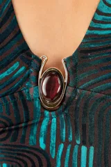 Traje de baño enterizo con escote en V profundo y detalle de aplique metálico con piedra en el centro. Presenta un diseño drapeado en la cintura y un estampado geométrico de ondas en tonos oscuros y turquesa.