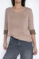 Sweater de tejido de punto color gris, con escote en V y mangas largas. Presenta un diseño liso en el exterior y un detalle de animal print en el interior de los puños, visible al doblarlos.
