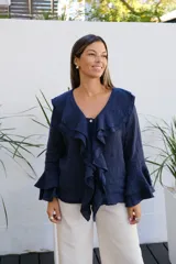 Blusa de lino color azul marino, con cuello con volados, cierre frontal con botones y mangas largas con puños acampanados de doble volado.