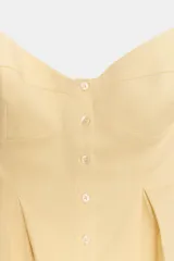 Top amarillo pálido con escote en pico, tirantes finos ajustables, detalle de pliegues en el bajo y cierre frontal con botones.