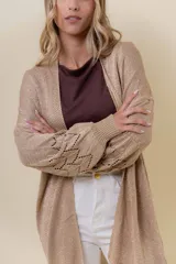 Cardigan tejido liviano color beige con efecto brillante y calados en las mangas. Diseño abierto y corte relajado.