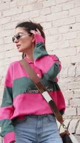 Sweater de hilo de algodón con diseño de rayas horizontales en color fucsia y verde oscuro. Posee cuello polo con botones de guampa y bordado frontal con el texto "Sierra Mora".