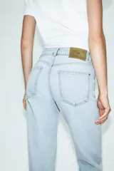 Jeans tipo mom fit de tiro alto color blanco, con diseño de cinco bolsillos, cierre frontal con cremallera y botón, y corte tobillero.