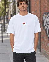 Remera blanca de algodón peinado, de corte recto y mangas cortas, con un pequeño estampado artesanal en el pecho que representa un hongo con elementos faciales.