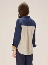 Camisa de lino color blanco con detalles combinados en tonos beige, cuello camisero, cierre frontal con botones oscuros y mangas largas con puños en contraste.