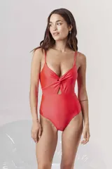 Traje de baño entero color rojo coral, con escote pronunciado en V y detalle de nudo fruncido en el centro del busto, dejando una abertura cut-out en el abdomen. Posee tirantes finos ajustables.