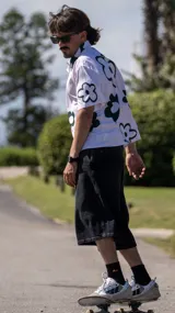 Camisa de manga corta, color blanco, con estampado de flores grandes en verde oscuro. Tiene cuello camisero y cierre frontal de botones.