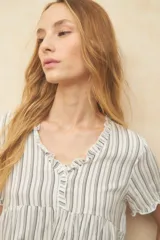 Blusa blanca con finas rayas verticales negras, de manga corta con volados y escote en V con pequeños botones y detalle de volado en el borde.