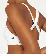 Top deportivo blanco de algodón orgánico con tirantes cruzados en la espalda y logo de minirayas.