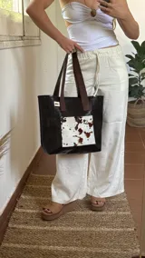 Bolso tote de ecocuero negro con bolsillo exterior de cuero vacuno con pelo, cierre superior y doble asa de cuero marrón.