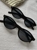 Lentes de sol modelo Soho con armazón ovalado de acetato negro brillante, detalles de tachas metálicas en las esquinas y cristales oscuros con protección UV400.