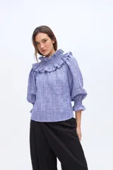 Blusa de algodón color celeste con textura rayada, cuello alto con efecto panal y volados, y mangas abullonadas con puños elásticos.