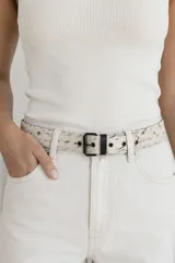 Cinto de cuero con estampado tipo animal print de vaca en tonos blanco y negro, hebilla metálica oscura y pasador negro.