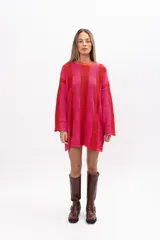 Buzo tipo poncho de tejido de punto con diseño de bloques de color en tonos rojo y fucsia. Presenta un corte oversize muy amplio, cuello redondo, mangas largas y bolsillos laterales integrados.