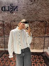 Camisa de corte clásico con estampado de rayas verticales en tonos celestes y marrones. Presenta volados delicados en el frente y en el cuello, cierre frontal con botones y mangas largas con puños ajustados.