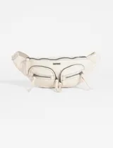 Riñonera de cuero sintético color beige, con diseño de dos bolsillos frontales con cierre y tiradores largos. Presenta herrajes metálicos oscuros y logo metálico en la parte superior.