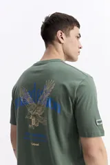 Remera de manga corta color verde militar, con escote redondo y ajuste regular. Presenta un estampado en la espalda con un águila en tonos dorados y azules, y texto en azul que dice "new season designed and produced by mistral".