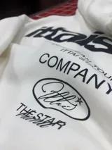 Hoodie de color blanco con capucha, diseño de corte holgado y estampado gráfico en la espalda con tipografía negra.
