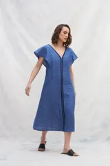 Vestido midi de lino en color azul, con escote en V tanto en el frente como en la espalda. Presenta mangas cortas con vuelo, silueta amplia y cintas verticales a contratono en el frente que estilizan la figura. Incluye bolsillos laterales.