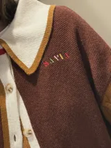 Cardigan de punto con diseño color block, cuello estilo polo en color rosado con borde rojo, cierre frontal con botones, manga derecha en verde oliva y manga izquierda en rojo, con puños y ruedo acanalados a rayas multicolor.