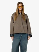 Campera de estilo worker color marrón topo, con cuello camisero y puños en contraste de color negro. Presenta cierre frontal con botones a presión metálicos, dos bolsillos frontales con solapa y diseño de corte holgado.
