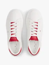 Zapatillas Tommy Hilfiger de diseño clásico y bajo, color blanco con detalles en rojo en la parte trasera del talón y en la lengüeta. Presentan cierre de cordones y el logo metálico distintivo de la marca en el lateral.