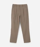 Pantalón de sastrería color beige, de corte holgado y diseño loose, con pliegues frontales, bolsillos laterales y cierre tradicional.