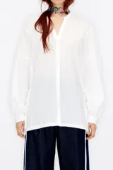 Blusa blanca de viscosa con cuello pico, manga larga y botonadura frontal.