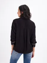Camisa de manga larga color malva, con cuello clásico, cierre frontal con botones y detalles de vivos negros en los puños.