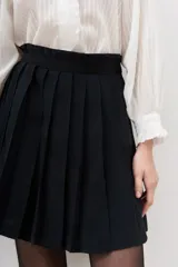 Falda corta negra plisada, de tiro alto con pretina ancha.