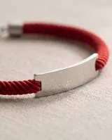 Pulsera de cordón rojo con chapa de identidad en acero y terminales metálicas.