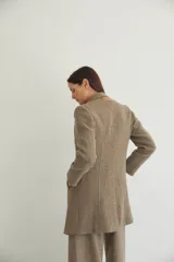 Saco corto entallado de lana fina, con cuello solapa, manga larga y cierre frontal con botones. Presenta un diseño clásico con textura de espiga en tonos tierra.