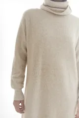 Vestido tipo sweater color beige, de tejido de punto acanalado, corte recto, largo a la rodilla y cuello alto.