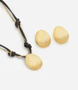 Conjunto de bijouterie compuesto por un collar y un par de aros. El collar presenta un cordón encerado oscuro con nudos decorativos, cadena metálica integrada y un dije ovalado con textura estriada. Los aros son de tipo clip o pasador, con el mismo diseño ovalado y acabado texturizado en tono dorado.