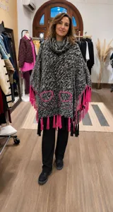 Poncho tejido de punto con cuello alto, diseño en gris jaspeado, bolsillos frontales con detalle de costura en fucsia y terminaciones de flecos en fucsia y negro.