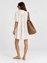 Vestido corto de lino natural, con cuello mao, mangas cortas abullonadas, cierre frontal con botones y pliegues decorativos en el pecho.