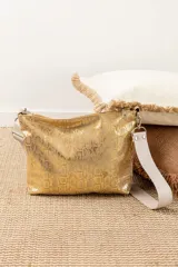 Cartera tipo sobre de color dorado con textura de piel de serpiente, cuenta con cierre superior y correa de hombro desmontable de tela en color crudo.