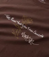 Remera boxy de algodón color marrón, con estampado trasero inspirado en Tupac y el concepto "The Rose", incluyendo texto y una imagen abstracta.