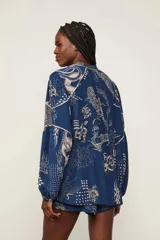 Blusa oversize azul con estampado integral en tonos claros, cuello en V con cordones ajustables, mangas largas abullonadas y puños elásticos.