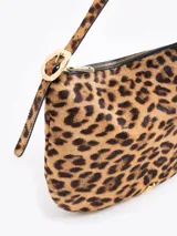 Cartera tipo hobo confeccionada en cuero con pelo vacuno estampado animal print. Presenta correa de hombro ajustable con detalles de hebillas metálicas en los laterales y cierre superior.