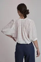 Camisa blanca con estampado de cruces, cuello mao y mangas 3/4 con detalle de pliegues en los hombros. Cierre frontal con botones.