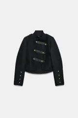 Chaqueta de estilo militar en color negro, con cuello redondo y cierre frontal mediante alamares decorativos. Presenta mangas largas con botones en los puños y forro interior a tono.