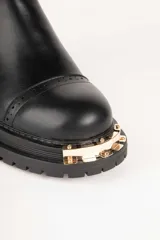 Bota Chelsea de cuero sintético color negro, con elástico lateral y aplique metálico dorado en la puntera.