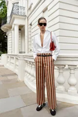 Pantalón de tiro alto y pernera recta con estampado de rayas verticales en tonos azul, marrón y beige. Incluye un cinturón delgado de color marrón oscuro con hebilla metálica dorada.