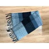 Bufanda rectangular de tejido grueso con diseño de cuadros en tonos azul, naranja, gris y beige, terminada con flecos en los extremos.