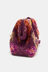 Bolso tipo sobre color violeta con diseño de abalorios y cuentas bordadas formando un patrón floral multicolor. Cuenta con una borla colgante en el cierre y correa de cadena extraíble.