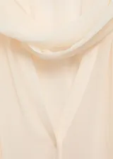 Blusa de viscosa color crema, con diseño semitransparente, cuello con lazada, mangas largas abullonadas y cierre frontal con botones.