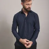 Camisa de vestir negra de manga larga, confeccionada en tejido técnico elástico y libre de arrugas, con cuello clásico y cierre frontal de botones.