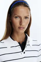 Jersey de punto blanco con rayas horizontales negras, cuello polo blanco y manga corta. Presenta una botonera frontal de tres botones negros.