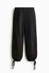 Pantalón tobillero negro de tejido arrugado, con cintura de tiro alto, pliegues delanteros y corte holgado de piernas barrel con elástico y cordón ajustable en los tobillos.